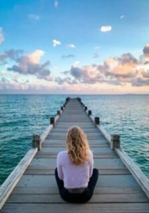 jeune fille assise sur la jetée en bois regardant la mer au loin. relaxation face à l'immensité.