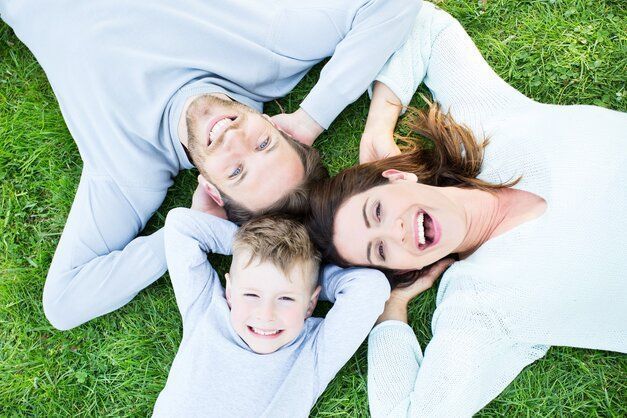 parents et enfants allongés dans l'herbe tête contre tète et main derrière la tête